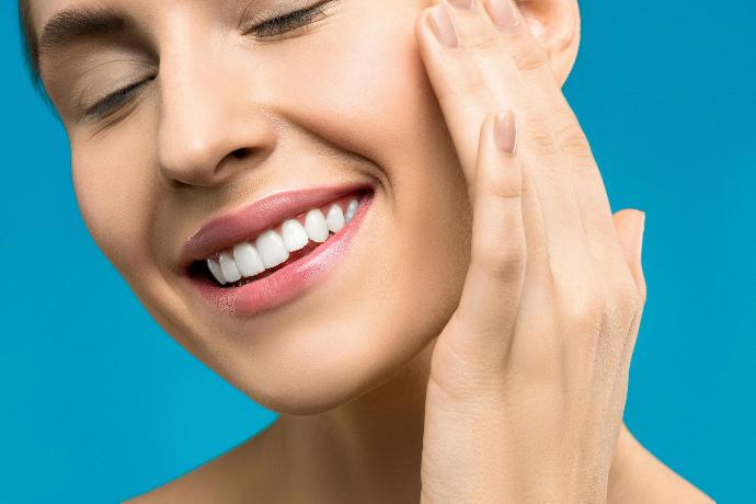 visage femme qui sourit et se touche la joue avec sa main