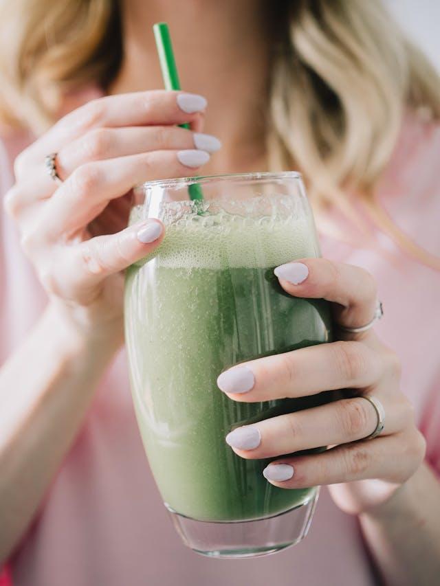 Femme avec gros plan sur ses mains qui tiennent un verre avec boisson verte et une paille verte