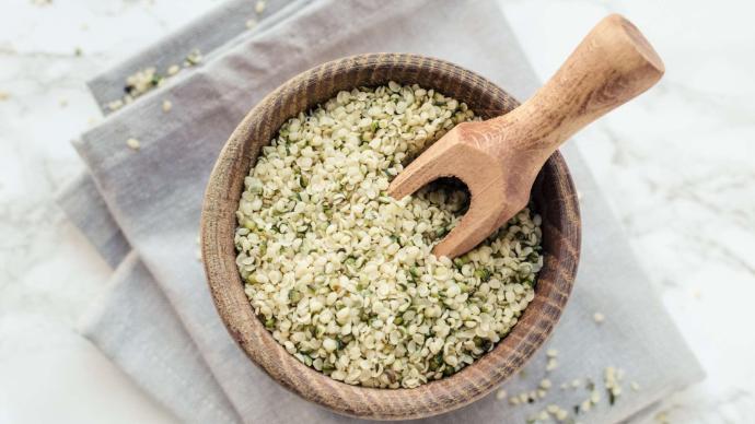 Graines de chanvre dans un bol en bois avec cuillère en bois posé sur un torchon gris clair