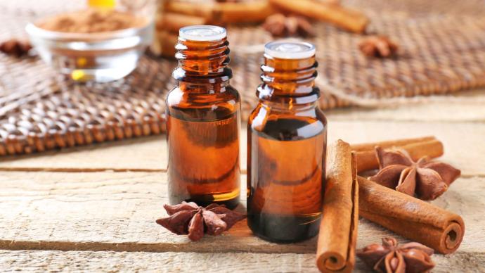 Two bottles of cinnamon essential oil with cinnamon sticks and stars on a table.