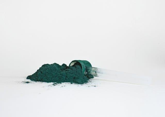 Spiruline en poudre qui sort d'une cuillère transparente sur fond blanc