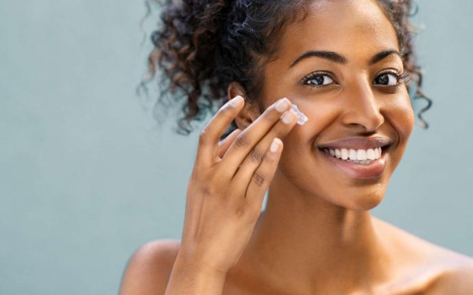 Femme noire qui sourit en se mettant de la crème sur la joue