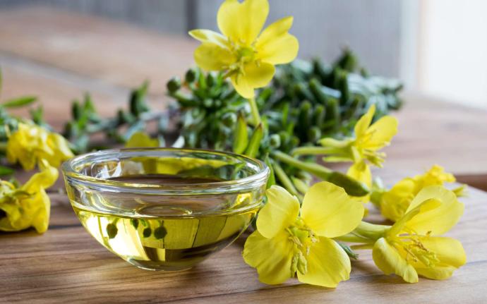 Huile végétale d'onagre dans récipient transparent avec des fleurs jaunes autour