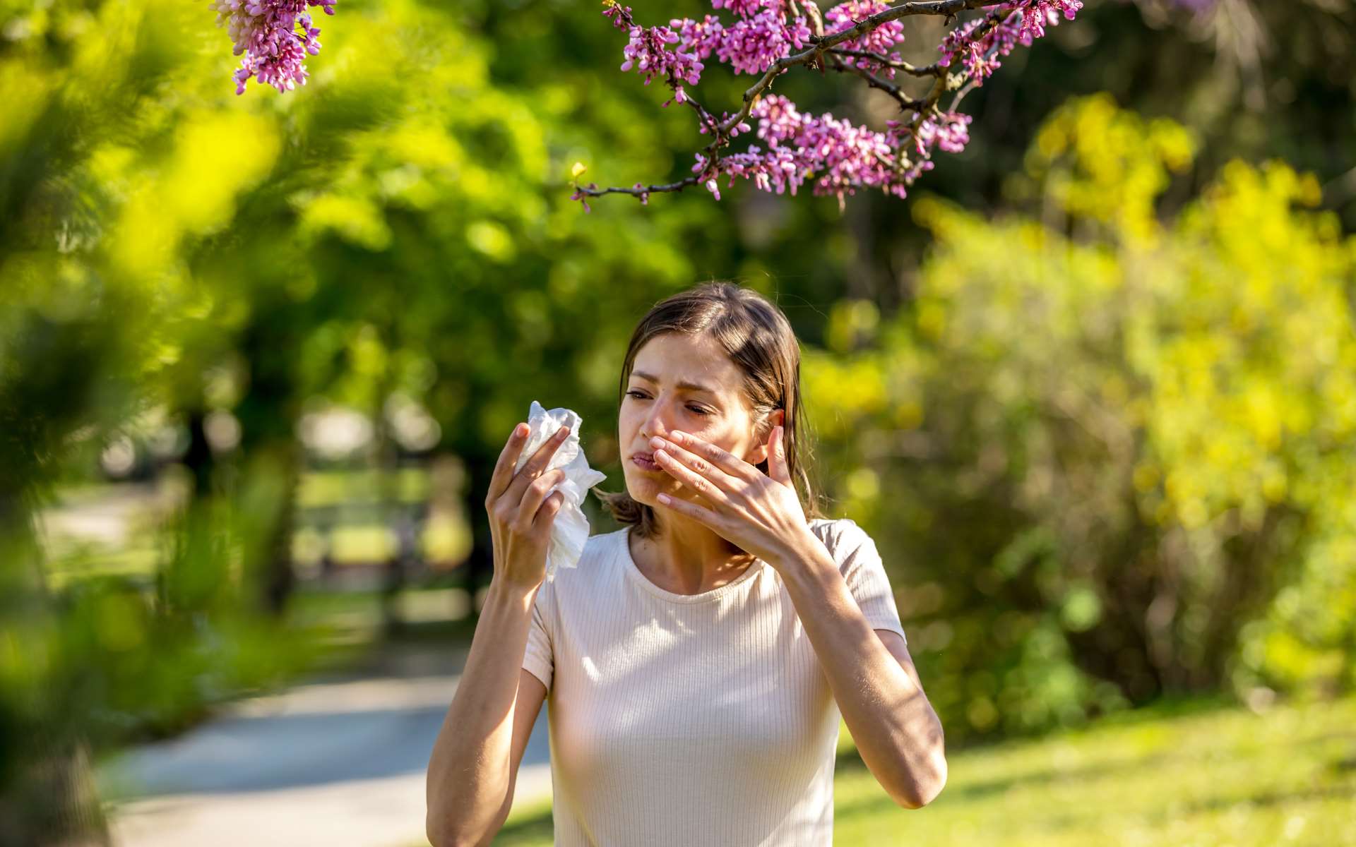 Jeune femme brune tee-shirt blanc avec un mouchoir blanc dans la main sous un arbre avec des fleurs roses