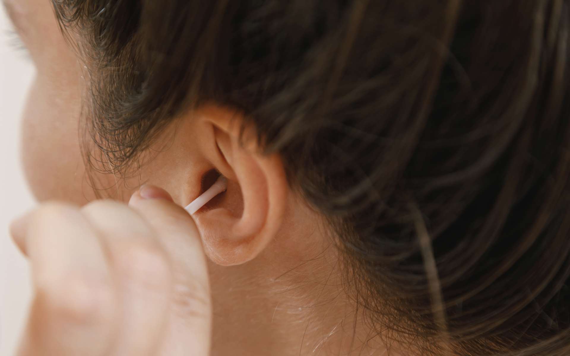 Visage femme brune trois-quart dos qui tient un coton-tige dans son oreille