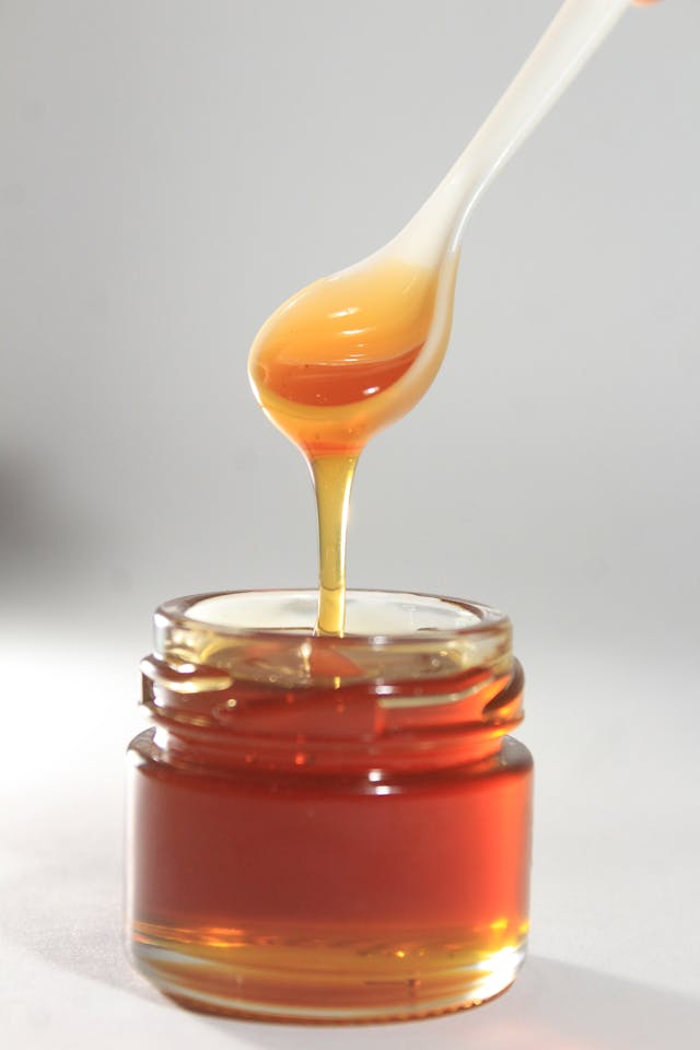 Pot de miel avec cuillère blanche au-dessus d'où coule du miel