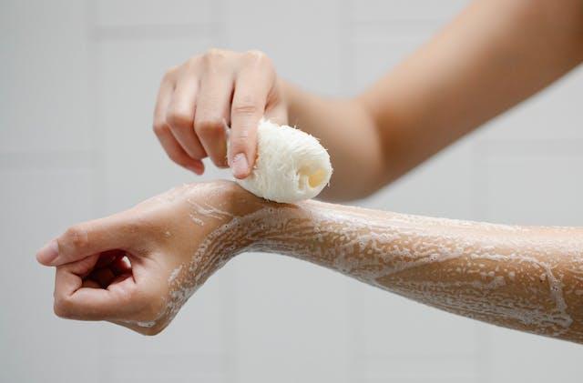 Bras de femme avec savon et l'autre main qui tient une éponge loofah