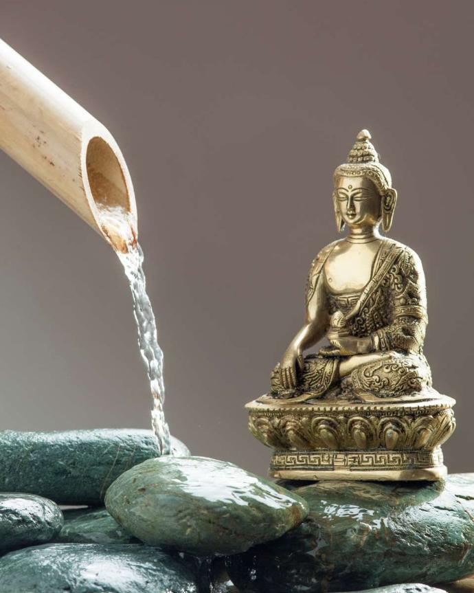 Buddha in gilded metal resting on wet stones with bamboo tube spouting water