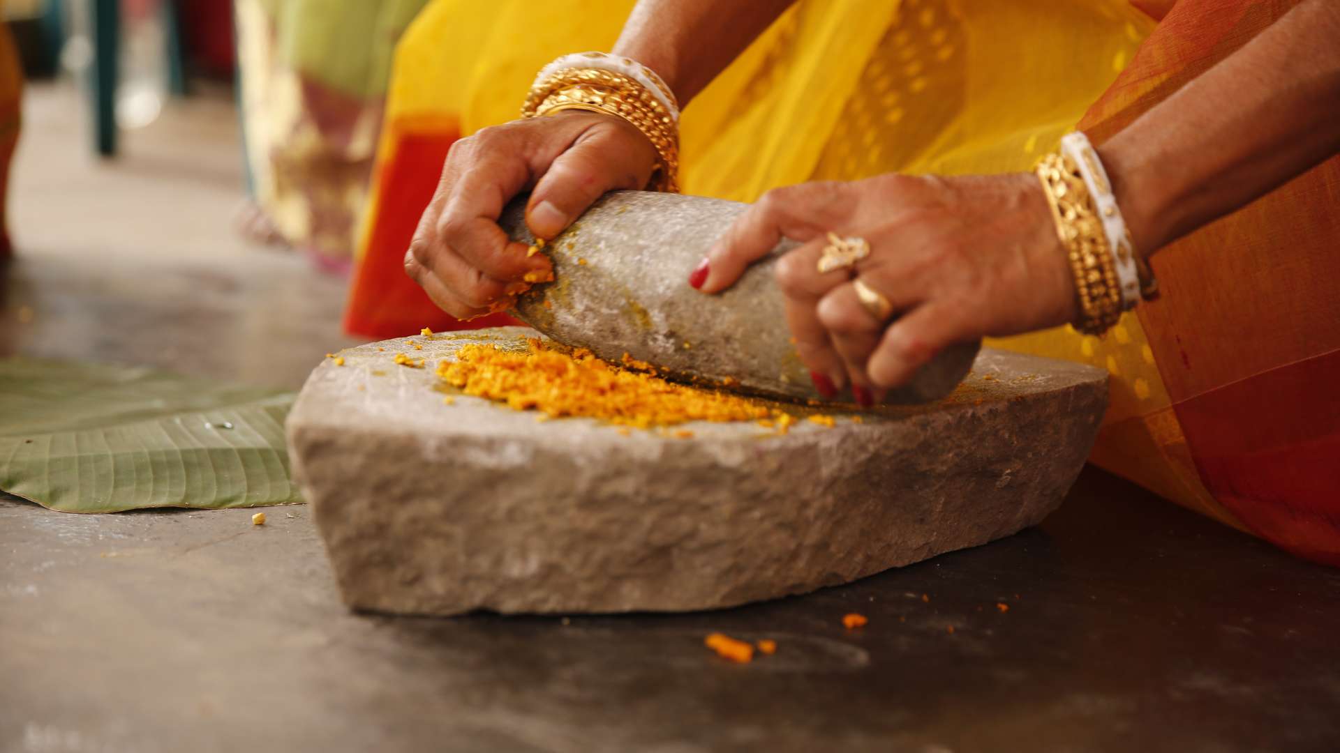 Femme avec des bagues et bracelets dorés qui pile du curcuma sur une pierre