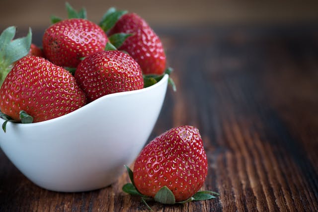 Aardbeien in een witte schaal met een aardbei ernaast op een donkere houten tafel