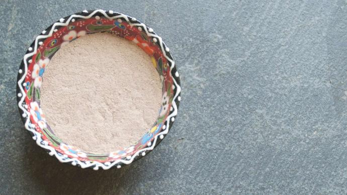 POudre de ghassoul dans ramequin coloré sur fond gris texturé