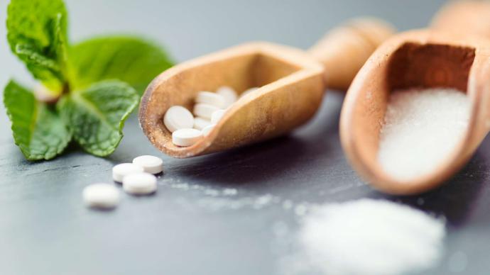 Xylitol solide et en poudre dans deux cuillères en bois avec des feuilles à côté