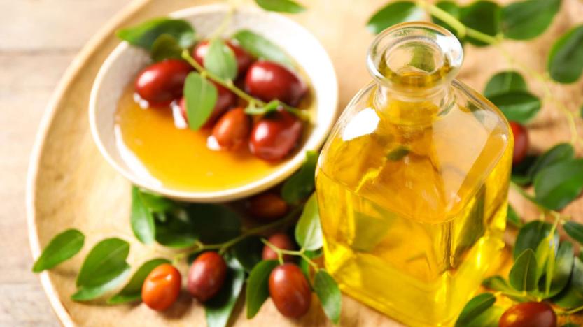 Bottle of vegetable oil with jojoba seeds and surrounding leaves