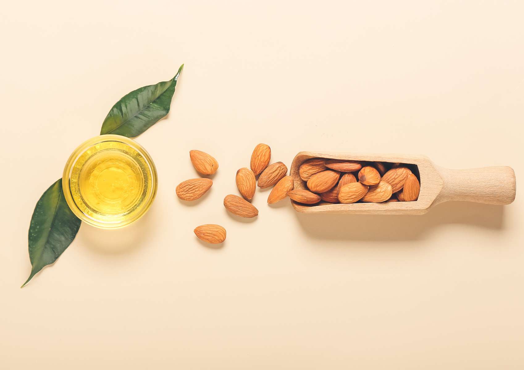 Pot d'huile d'amande avec feuilles et à côté des amandes dans une cuillère en bois et sur le fond abricot pâle