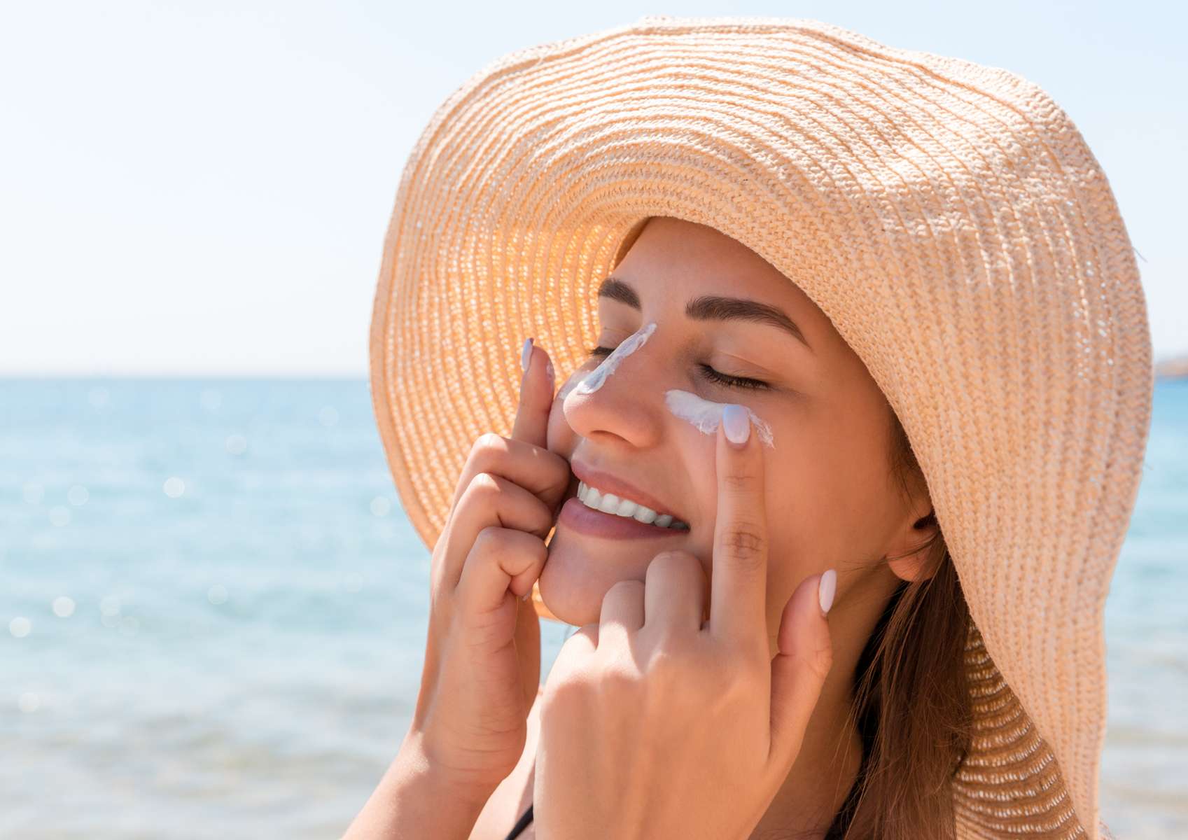 Femme sous avec chapeau de paille et crème solaire sur le nez qui se met de la crème solaire sur les joues