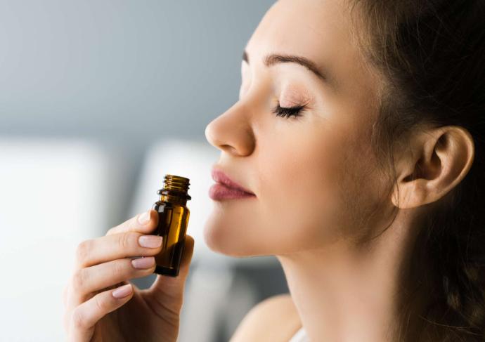Woman in profile, eyes closed, breathing over a bottle of essential oil in her hand.