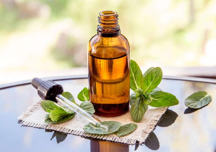 Brown bottle of essential oil on a glass table with pipette and mint leaves next to it