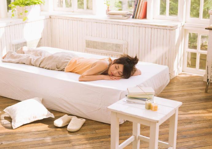 Woman lying on her stomach on a white bed, napping with a coffee table beside her.
