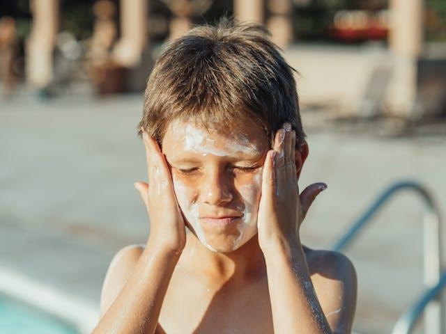 Jeune garçon qui se met de la crème solaire sur les joues