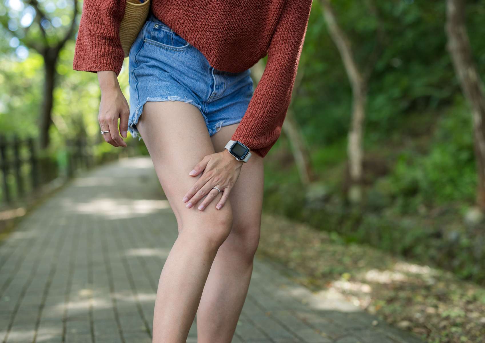Femme en short en jean et pull rouille qui se gratte la jambe