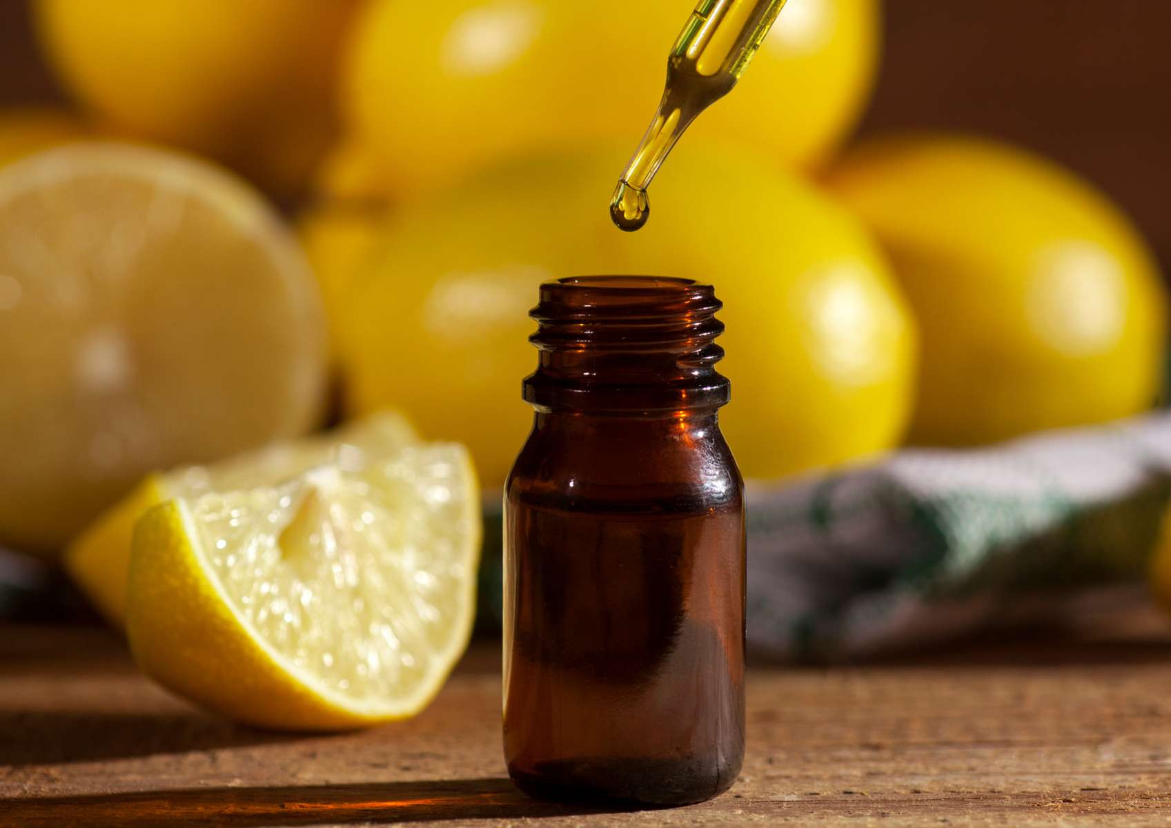 Flacon d'huile essentielle avec pipette au-dessus et citrons en arrière-plan sur une table en bois