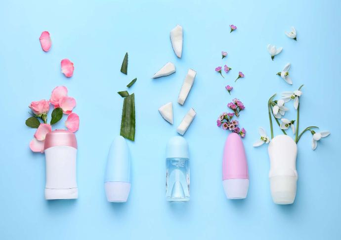 Vijf deodorants op een rij met bloemen, aloë vera en kokosnootstukjes op een blauwe achtergrond