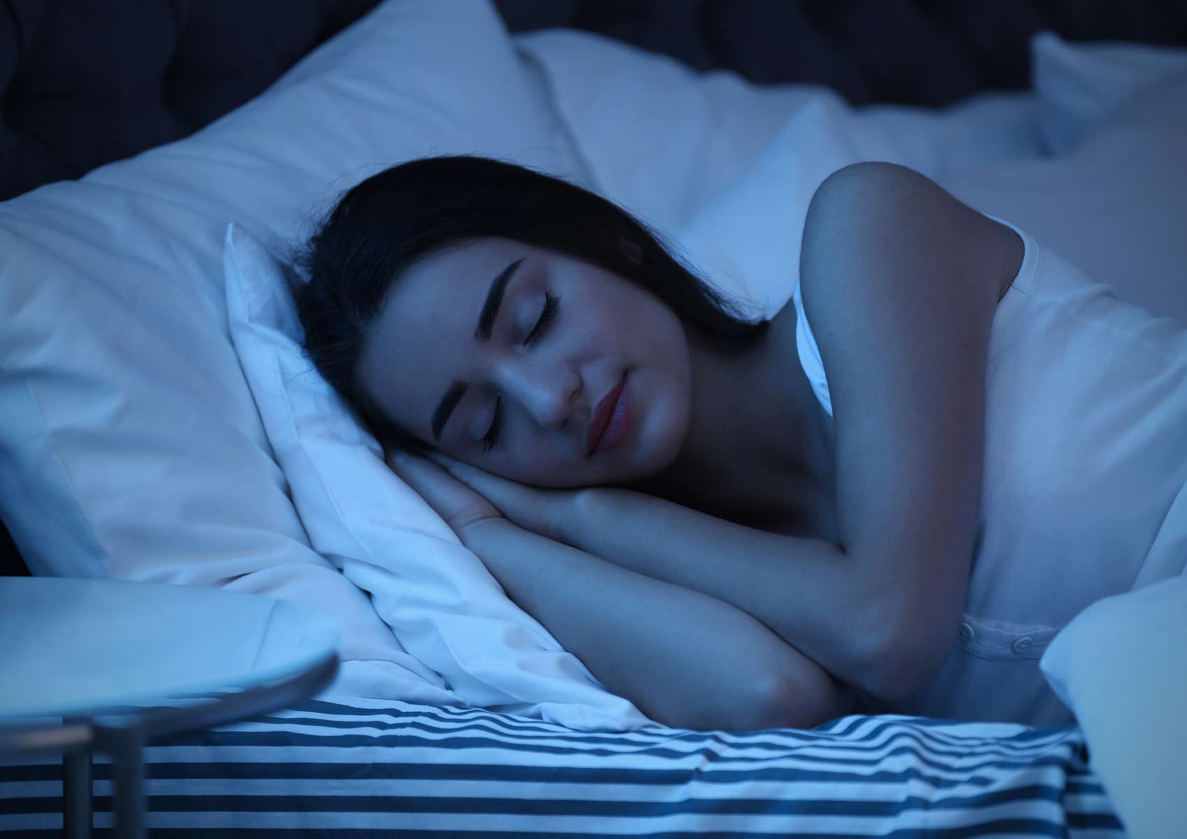 Jeune femme brune qui dort sur le côté avec oreillers blanc et drap housse à rayures