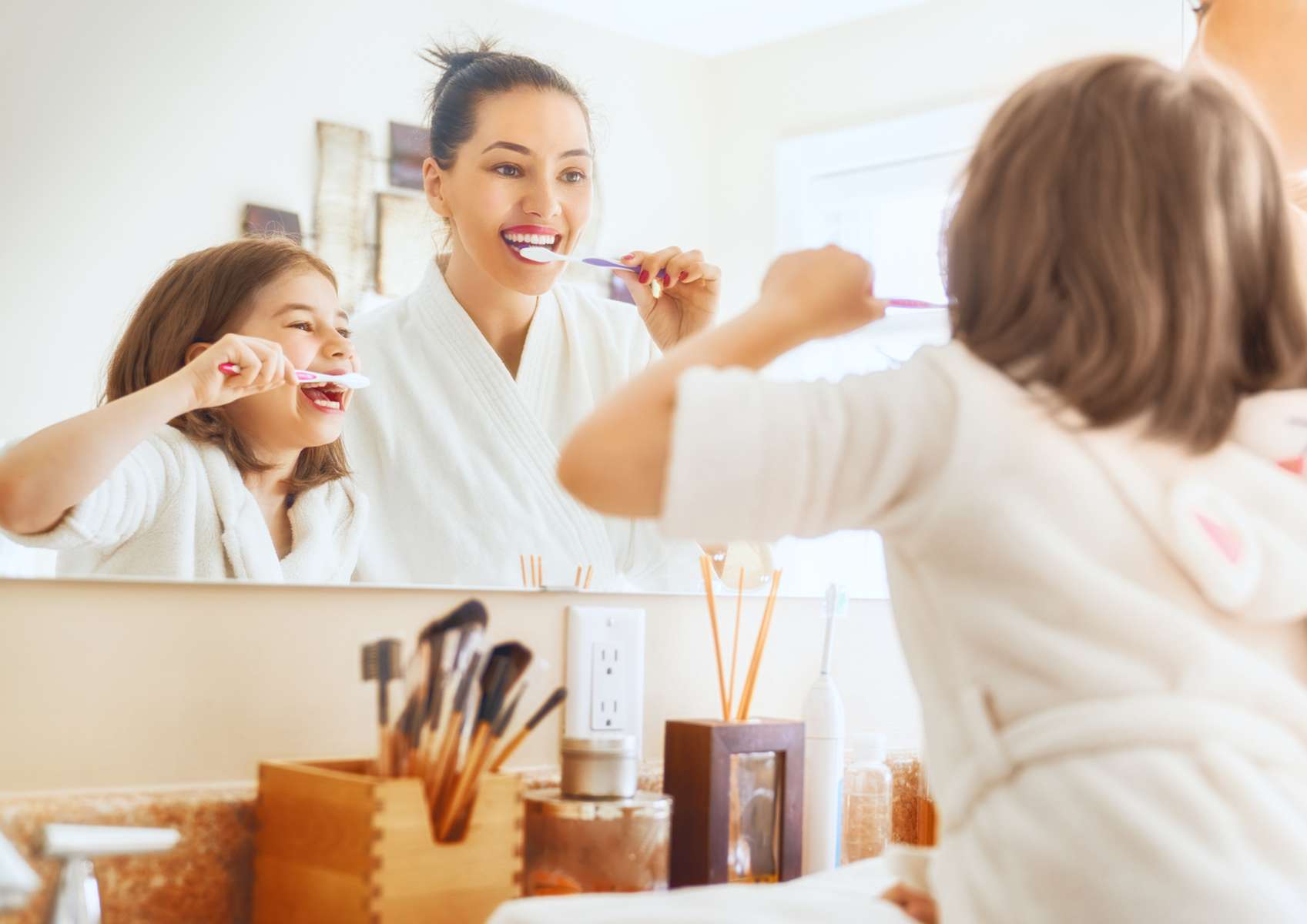 Jeune maman et sa petite fille en peignoirs blancs qui se brossent les dents devant miroir salle de bains