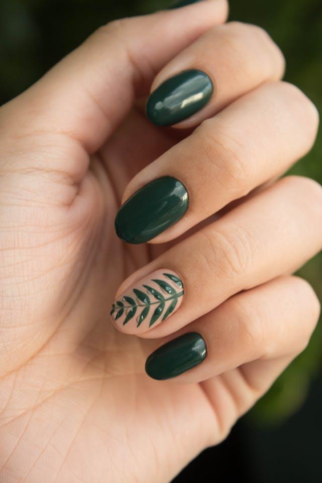 Main avec ongles vernis vert sapin et nail art feuille sur l'annulaire