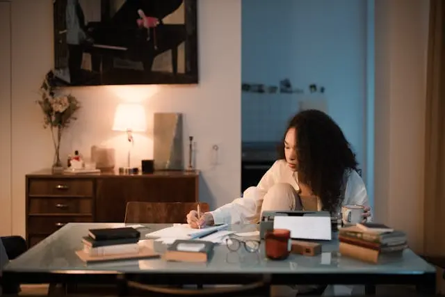 Jeune femme noire concentrée qui écrit sur un bureau sur une table avec livre et machine  à écrire dans une salle à manger