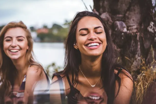 Deux jeunes femmes blonde et  brune qui sourient avec tronc d'arbre et plan d'eau en arrière-plan