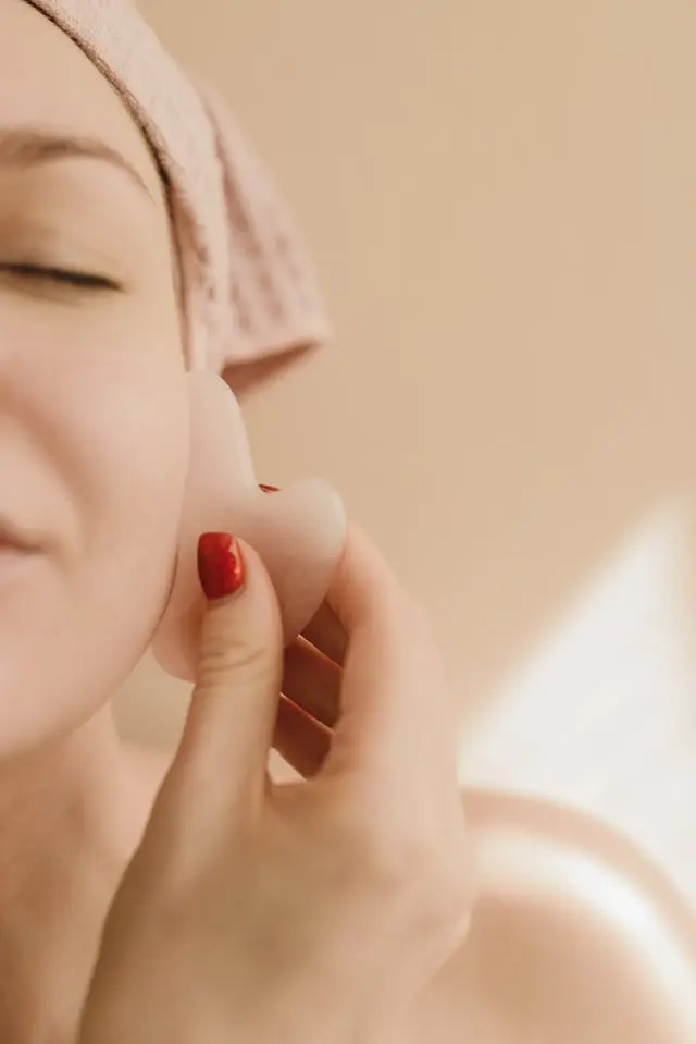 Femme qui tient un gua sha en quartz rose sur sa joue sur fond beige