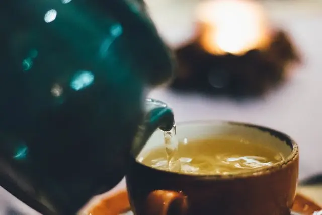 Thé versé d'une théière dans une tasse avec feu de cheminée en arrière-plan