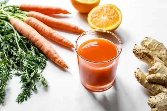 Jus de carotte dans un verre avec des carottes, citrons et gingembre
