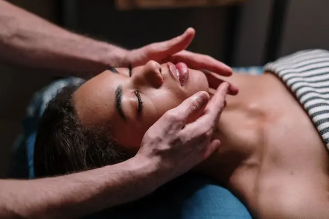 Massage kobido visage jeune femme noire avec serviette rayée noire et blanche sur  le buste les yeux fermés