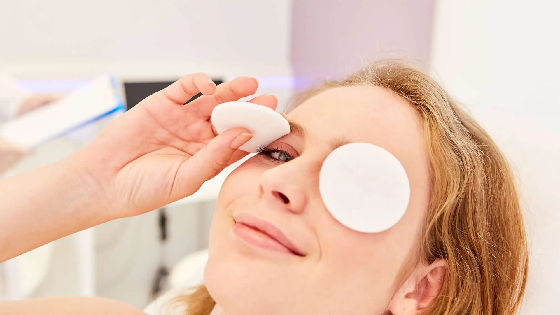 Visage jeune femme blonde qui sourit une compresse sur l'œil gauche et une autre dans sa main au-dessus de l'œil droit