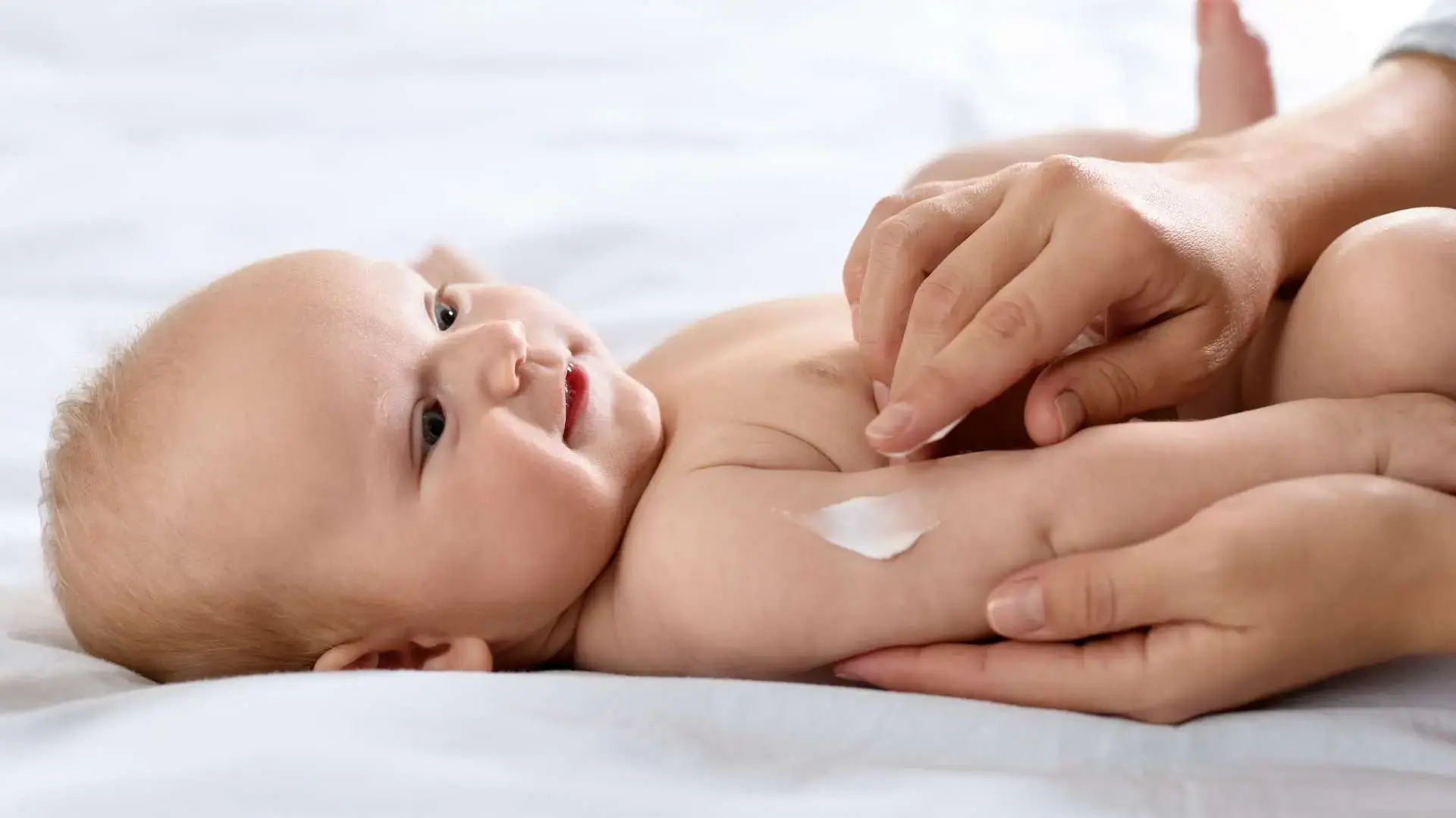 Bébé allongé sur le dos avec  main qui applique de la crème sur son bras droit
