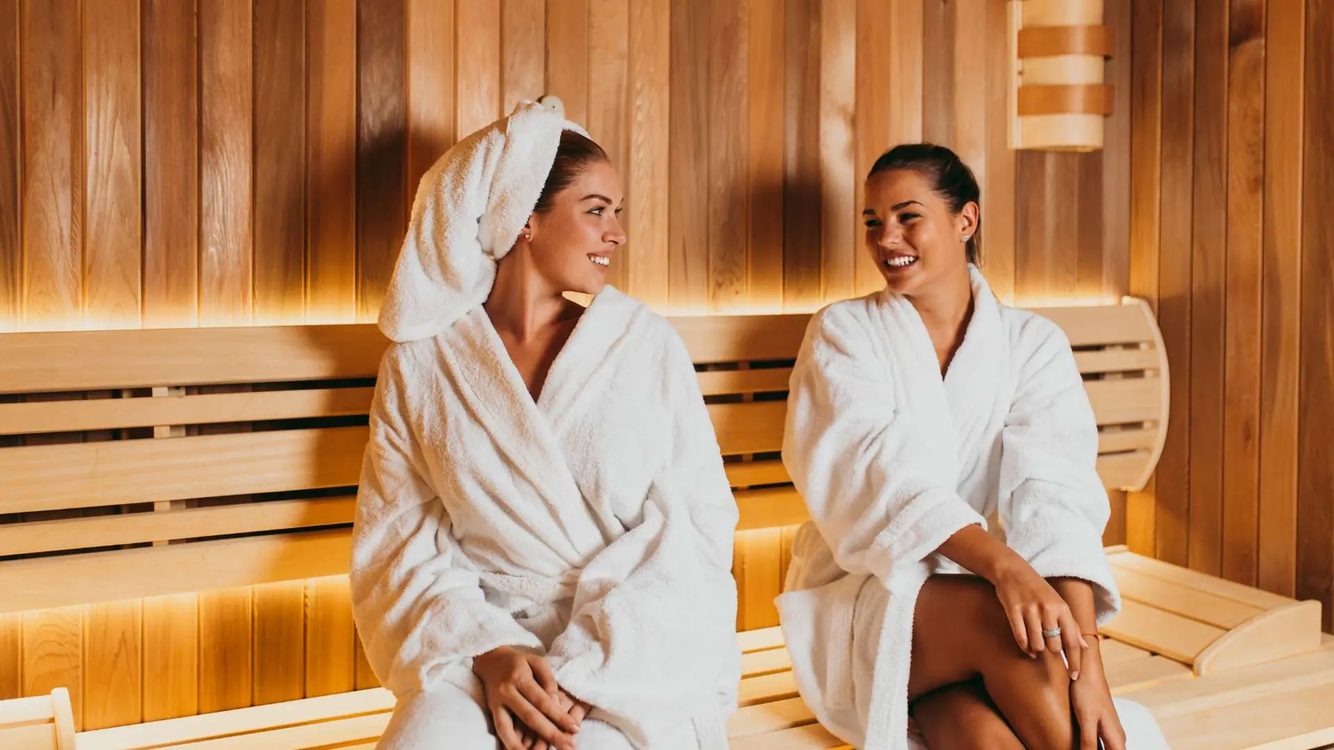 Deux jeunes femmes en peignoir blancs qui sourient dans un  sauna