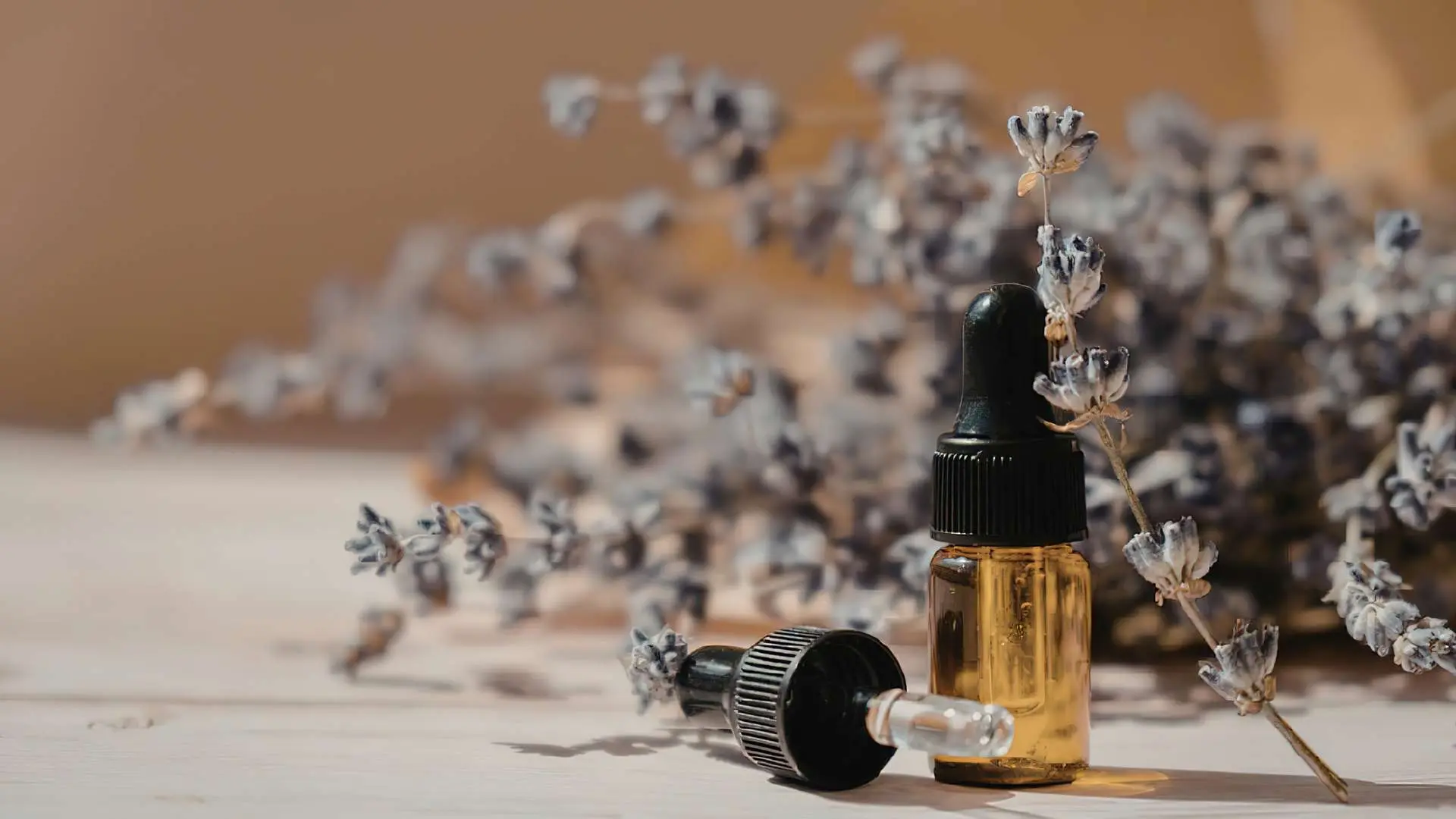 Flacon d'huile essentielle avec de la lavande derrière posés sur une table