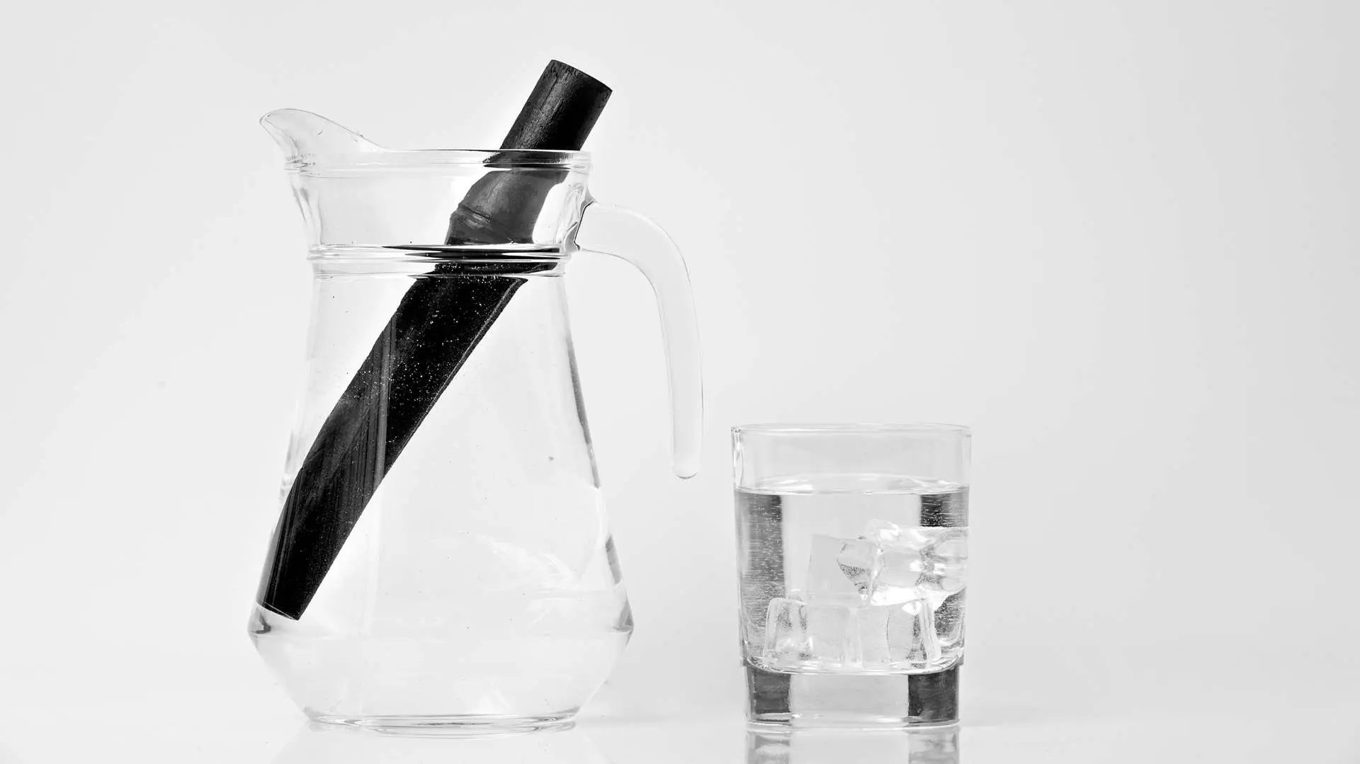 Bâtonnet charbon actif dans carafe d'eau avec  verre d'eau avec des glaçons à côté
