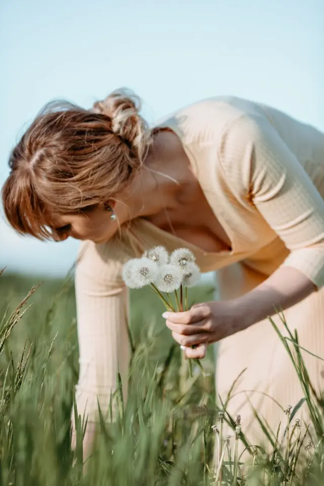 Femme penchée vers de l'herbe qui tient des pissenlits dans la main