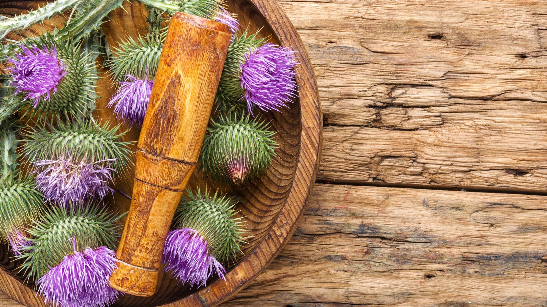 Vue de haut assiette en bois avec pilon en bois et chardons-Marie posée sur table en bois rustique