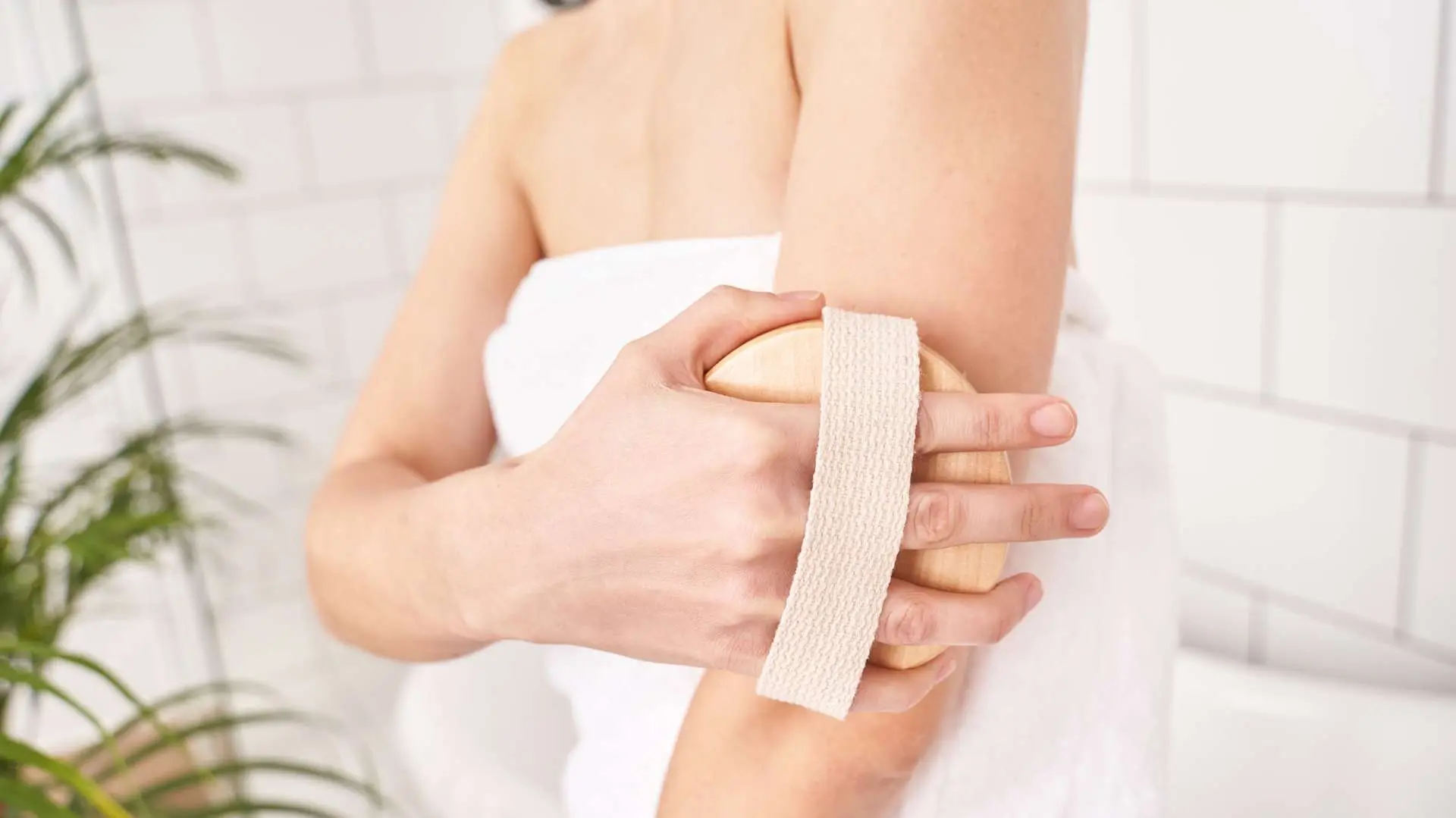 Gros plan brosse de drainage lymphatique sur un bras enue par une main de femme avec serviette blanche autour du  buste