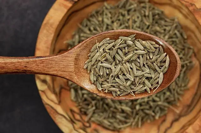 Vue de haut cuillère en bois avec graines de cumin  au-dessus d'une assiette en bois avec des graines de cumin