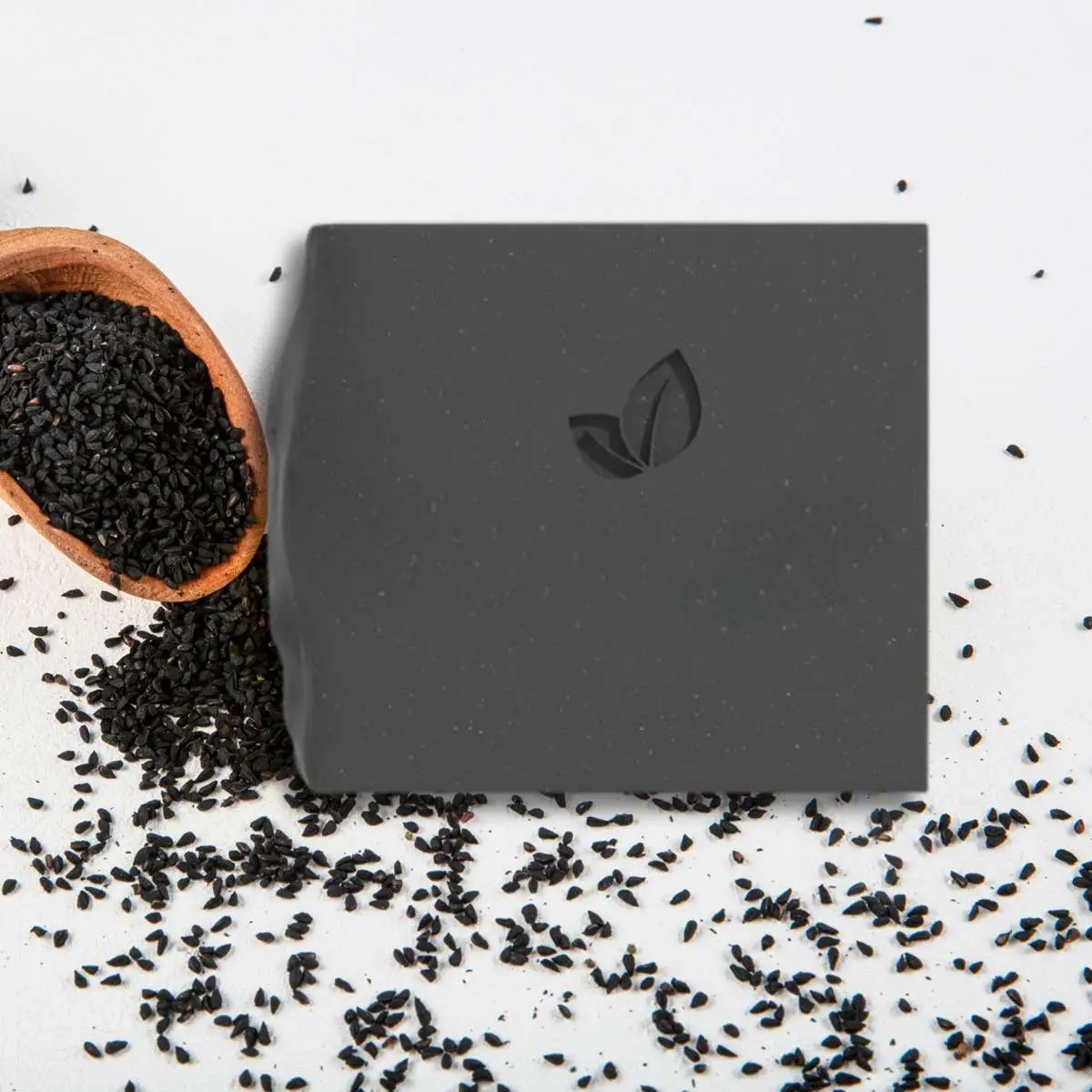 Vue de haut savon à l'huile de nigelle bio SUn & Sia avec graines de nigelle noires dans cuillère en bois et autour sur fond blanc