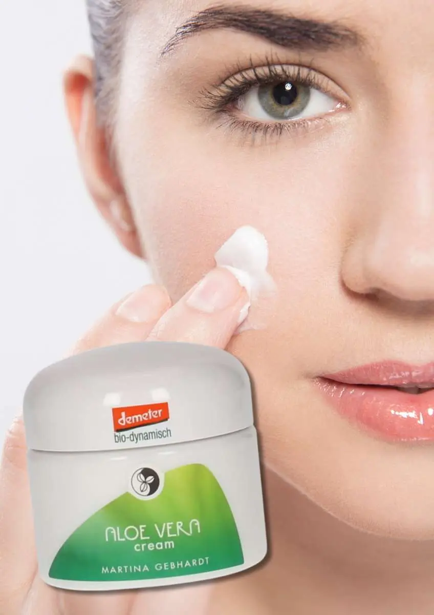 Gros plan visage de femme qui s'applique de la crème sur la joue droite avec pot de crème aloe vera Martina Gebhardt