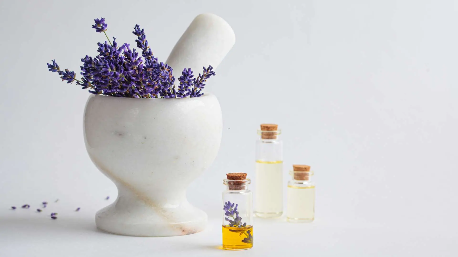 A white marble mortar with lavender inside and three bottles of essential oil, one of which contains a sprig of lavender
