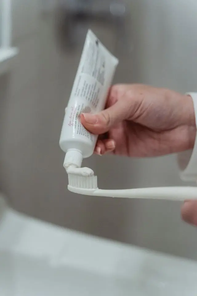 Main de femme tenant un tube de dentifrice et étalant du dentifrice sur sa brosse à dents blanche en plastique