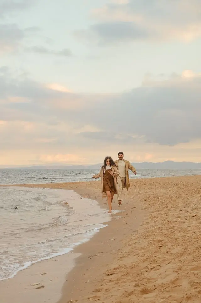 Couple habillés en beige et blanc courant sur  la plage au bord de l'eau