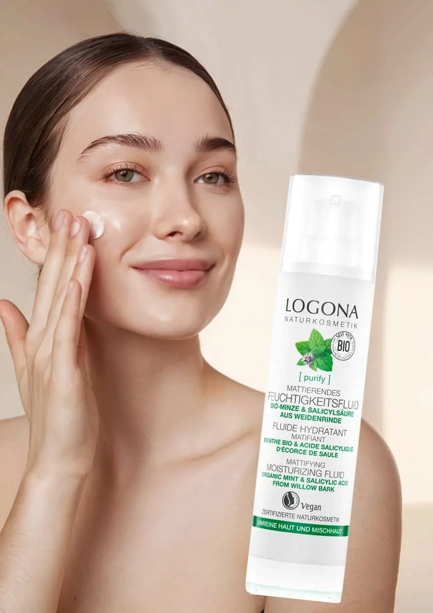 Jeune femme qui sourit  en s'appliquant de la crème sur la jour avec flacon de fluide hydratant et matifiant Purify Logona